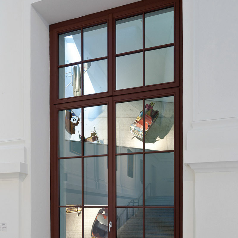Bildfüllend: dunkelbraunes Sprossenfenster mit sehr dünnen Sprossen innerhalb der zwei Flügel und des Oberlichts in weißer Fassade