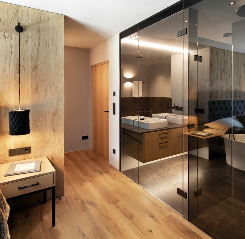 Badezimmertüren aus grauem Glas, in denen sich ein Doppelbett im Schlafzimmer und andere Teile des Badezimmers spiegeln.