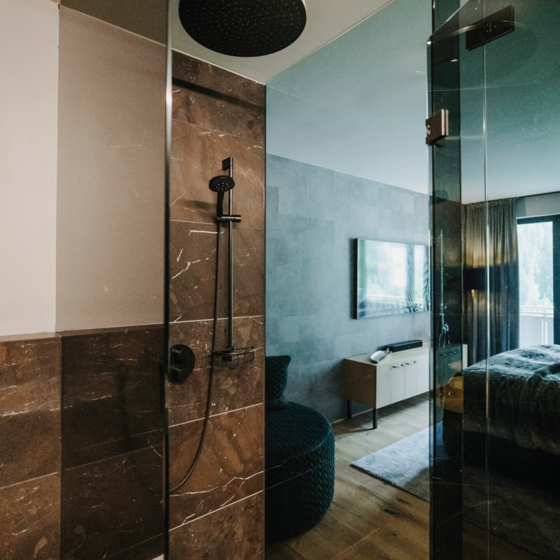 Badezimmertüren aus grauem Glas, in denen sich ein Doppelbett im Schlafzimmer und andere Teile des Badezimmers spiegeln.