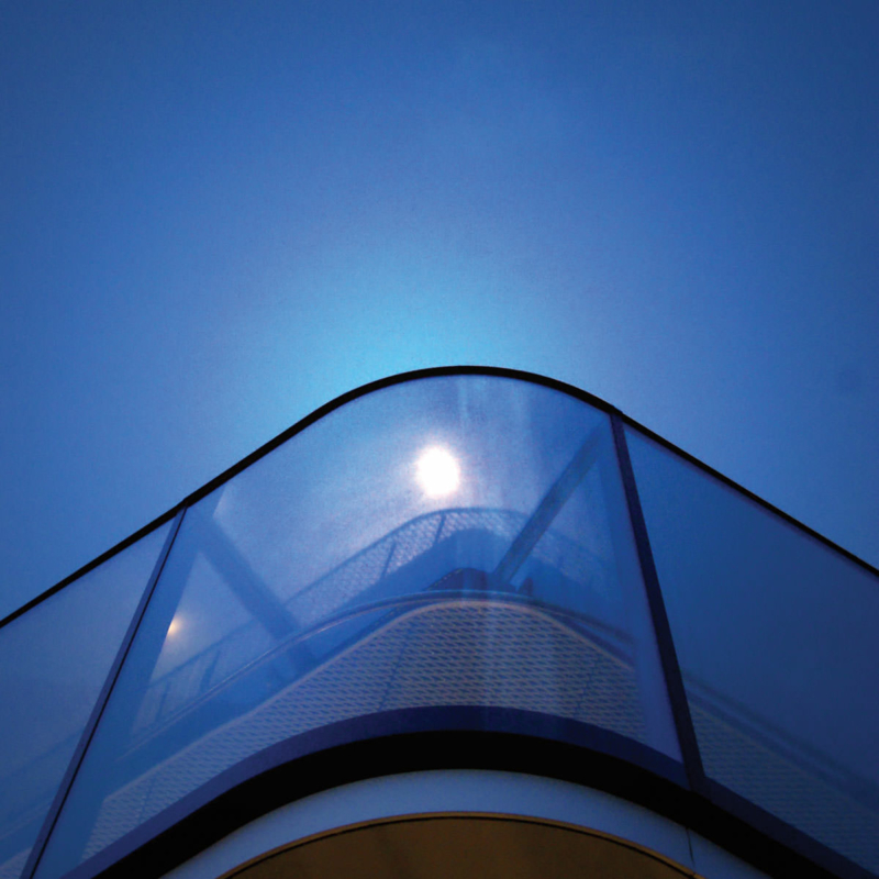 Sicht von schräg unten auf eine blau schimmernde gebogene Ecke eines Glasgeländers vor blauem Abendhimmel