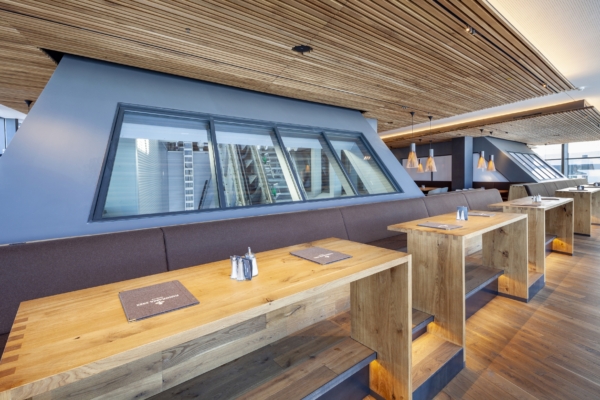 Holztische vor unterschiedlich geformten Fensterscheiben aus Brandschutzglas im Restaurant der Bergstation Zugspitze