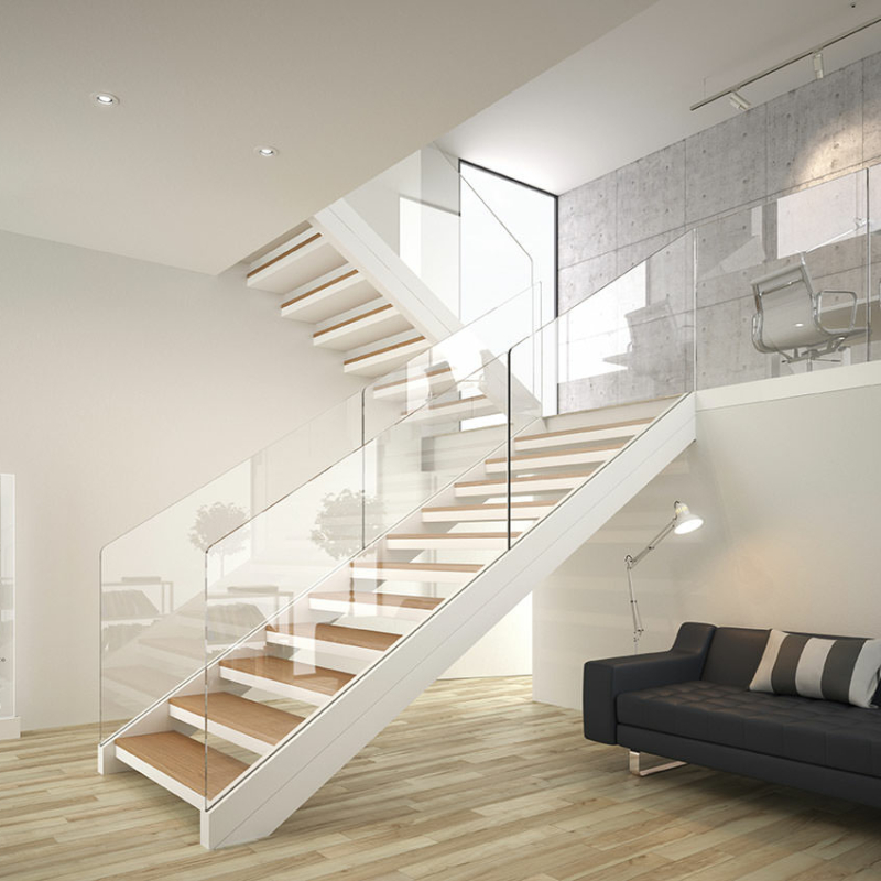 Offenes Treppenhaus in Weiß mit Ganzglasgeländern an der Treppe und der Brüstung oben. Unten rechts ein dunkelgraues Sofa.