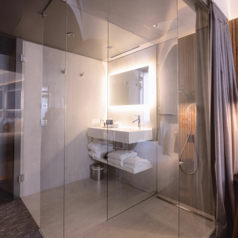 Badbereich in einem Hotelzimmer mit gebogener Duschabtrennung aus Glas.