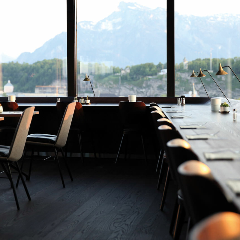Restaurant mit großen Glasfenstern und Blick auf Salzburg und Berge.