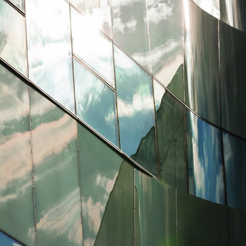 Fassadenausschnitt mit gläsernen, rechteckigen Fassadenplatten, in denen sich der Himmel spiegelt.
