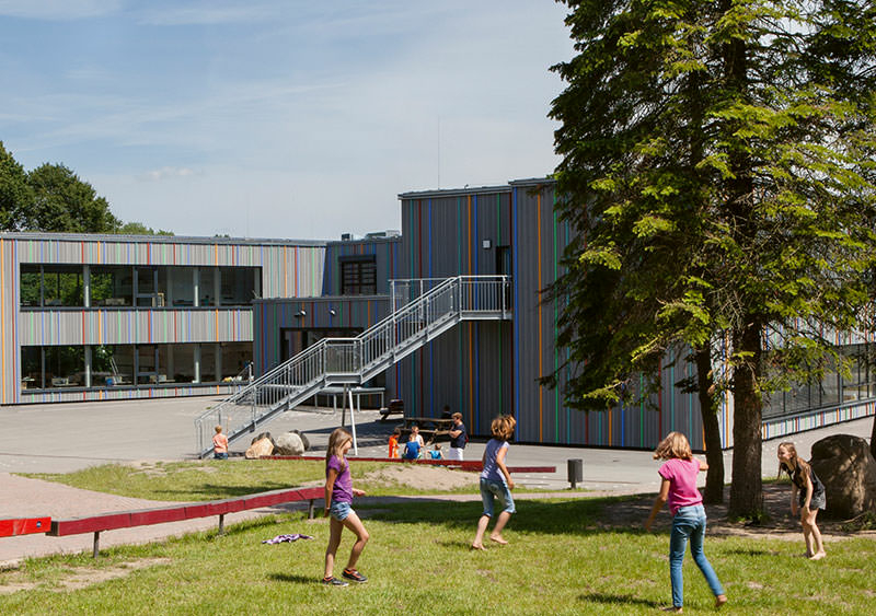 Ein grau-bunt gestreiftes Schulgebäude mit zwei Flügeln