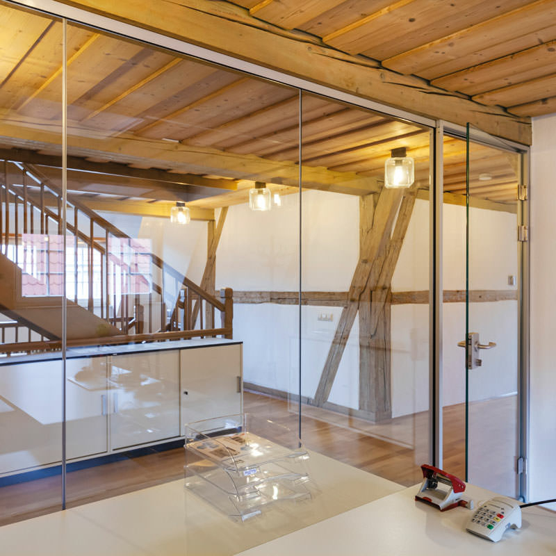 Ein Büro mit einer Ganzglaswand zu einem Flur mit Treppe in einem Fachwerkgebäude. [Bild 4]: _MG_8702.jpg