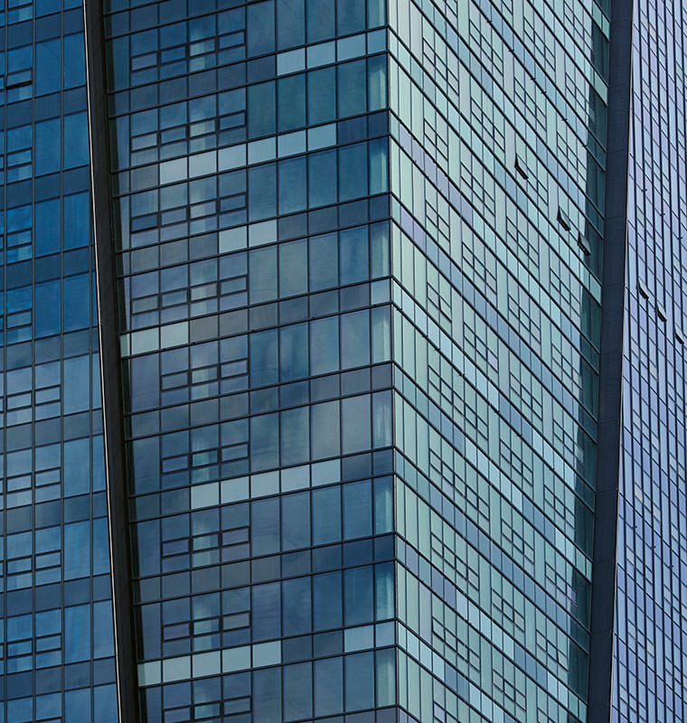 Blick auf einen Teil der Glasfassade des Nivy Tower mit verschiedenfarbigen Glasfeldern. Die unterschiedlichen Reflexionsgrade der Beschichtung lassen den Farbton grünlich bis bläulich schimmern.