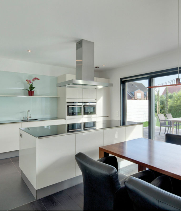 Offener Küchenbereich mit Glasrückwand, freistehender Arbeitstheke und großem Esstisch vor einer Terrassentür