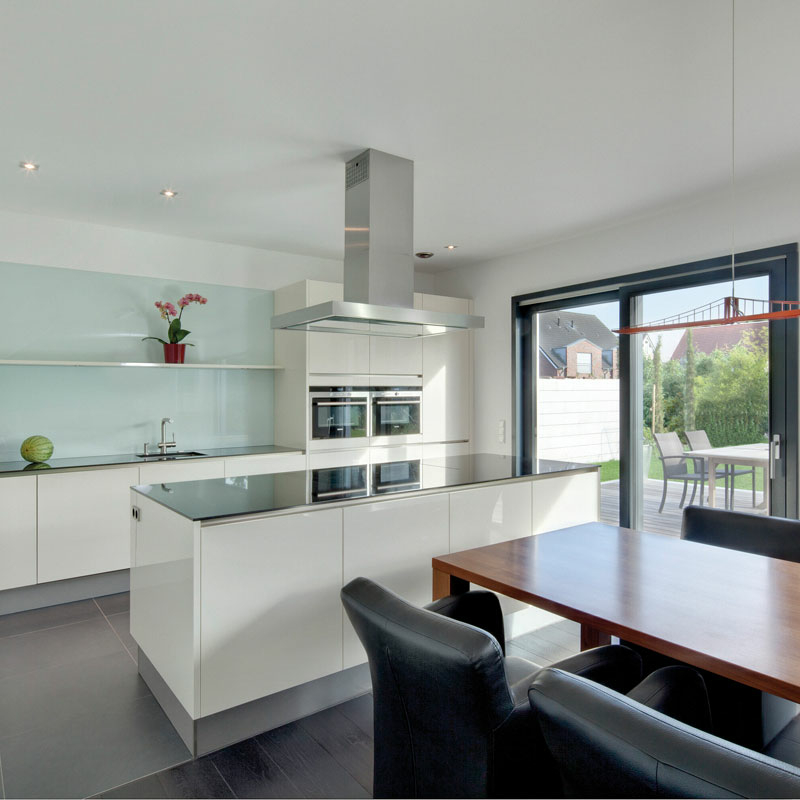 Offener Küchenbereich mit Glasrückwand, freistehender Arbeitstheke und großem Esstisch vor einer Terrassentür