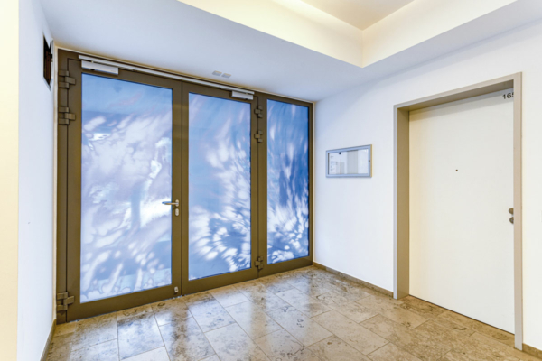 Blick auf eine dreiflügelige, mit einem Himmelsmotiv bedruckte Brandschutztür: weiße Wolken vor strahlend blauem Hintergrund