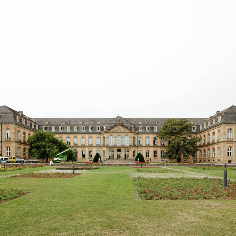 Frontalansicht des Neues Schlosses Stuttgart mit seinem zweistöckigen Hauptgebäude mit zwei rechtwinklig davon abgehenden Flügeln. Die klassische Lochfassade prägen rechteckige Fenster