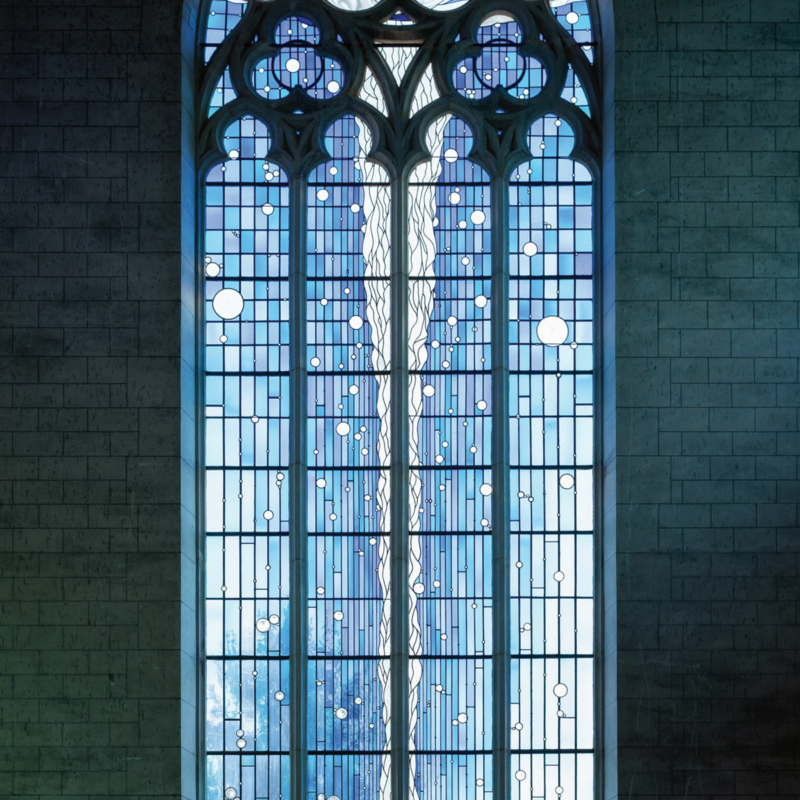 Schmales hohes Kirchenfenster mit vielen kleinen Gläsern in unterschiedlichen Blautönen