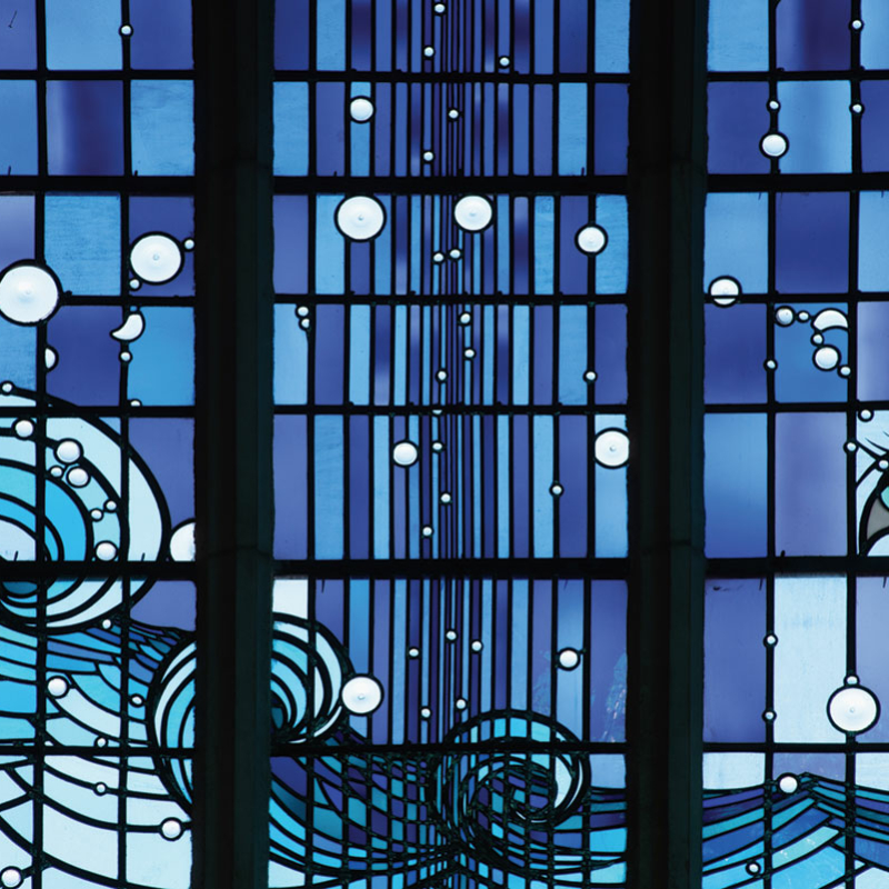 Teil eines Glasfensters aus vielen kleinen Gläsern in unterschiedlichen Blautönen, mit abstrahierten Wellen und anderen Motiven