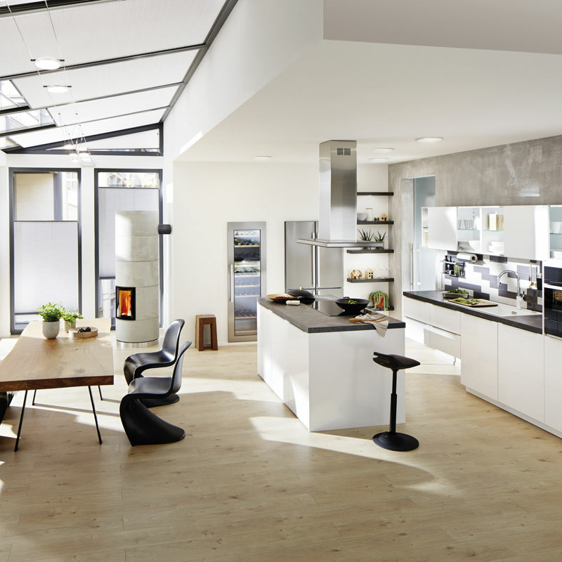 Offener Küchenbereich mit Wintergarten, freistehendem Arbeitsblock, Holztisch mit schwarzen Stühlen und Küchenzeile mit Rückwand aus grau-weißem Glas