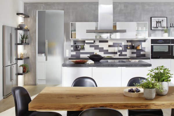 Blick auf eine Küchenzeile mit grau-weiß gemusterter Rückwand aus Glas neben einer halbgeöffneten Ganzglastür