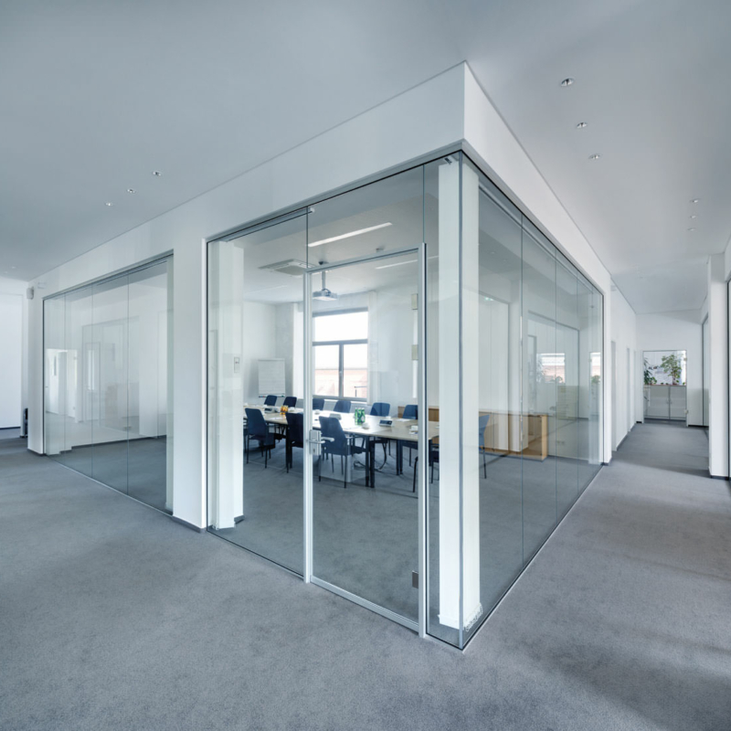 Große Glaselemente in weißen senkrechten Rahmen trennen einen separaten Bereich in einem Großraumbüro ab.