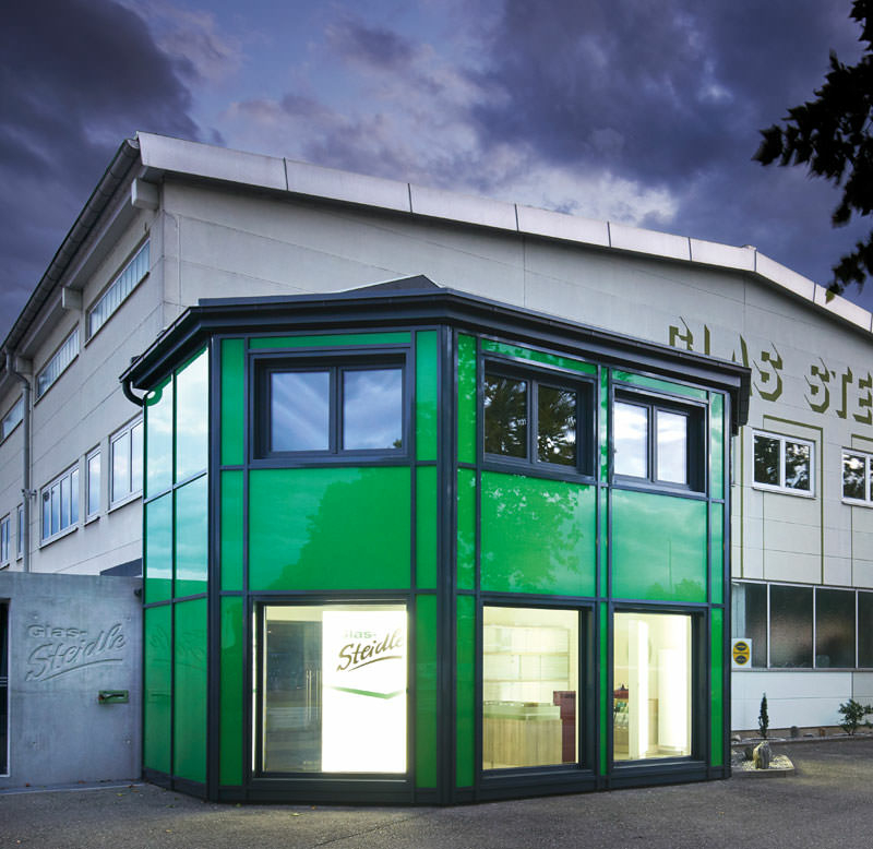 Firmengebäude von Glas Steidle mit einem vorgesetzten Eingangsbereich, der eine Fassade aus grünem Glas hat.