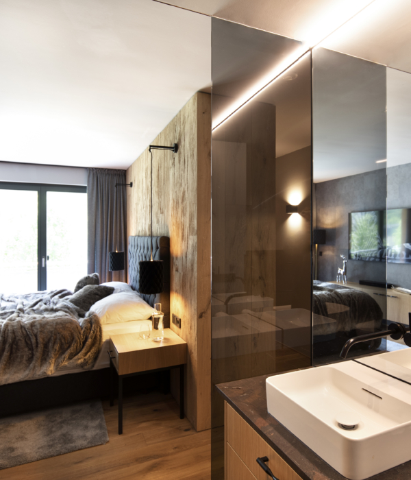 Blick aus einem Badezimmer mit geöffneter Tür aus grauem Glas auf ein Doppelbett