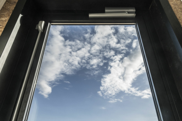 Blick schräg nach oben aus einer Glastür in einen Himmel mit wenigen Wolken