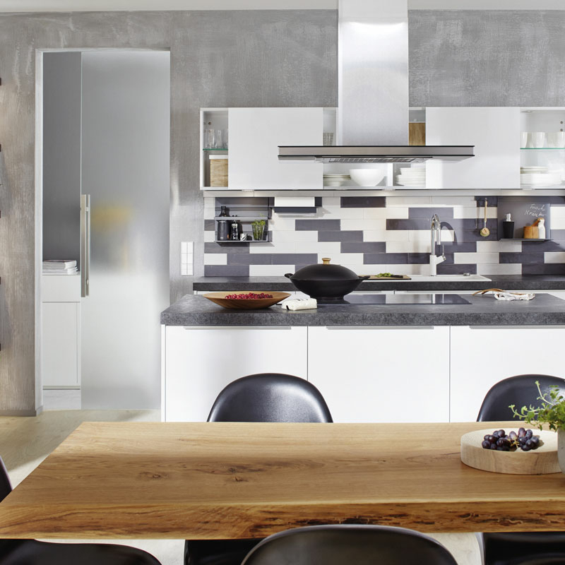 Blick auf eine Küchenzeile mit grau-weiß gemusterter Rückwand aus Glas neben einer halbgeöffneten Ganzglastür