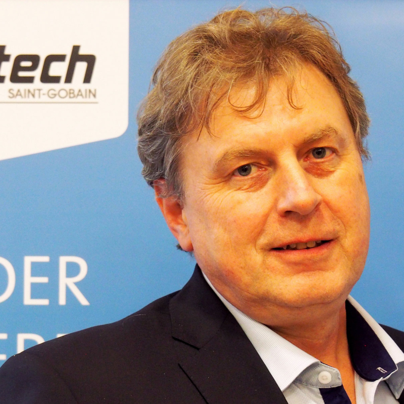 Porträtfoto von Christoph Baier, Vertriebsleiter Deutschland von Vetrotech Saint-Gobain, vor einer Stellwand in den Vetrotech-Farben blau und weiß, links oben im Bild ist das Vetrotech-Logo sichtbar.