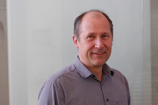 Thomas Kerscher, Geschäftsführer der Amberger Glas GmbH, blickt den Betrachter leicht zu seiner linken Seite abgewendet an. Er trägt ein am obersten Knopf offenes, kleinkariertes Hemd und steht vor einem hellen Hintergrund.