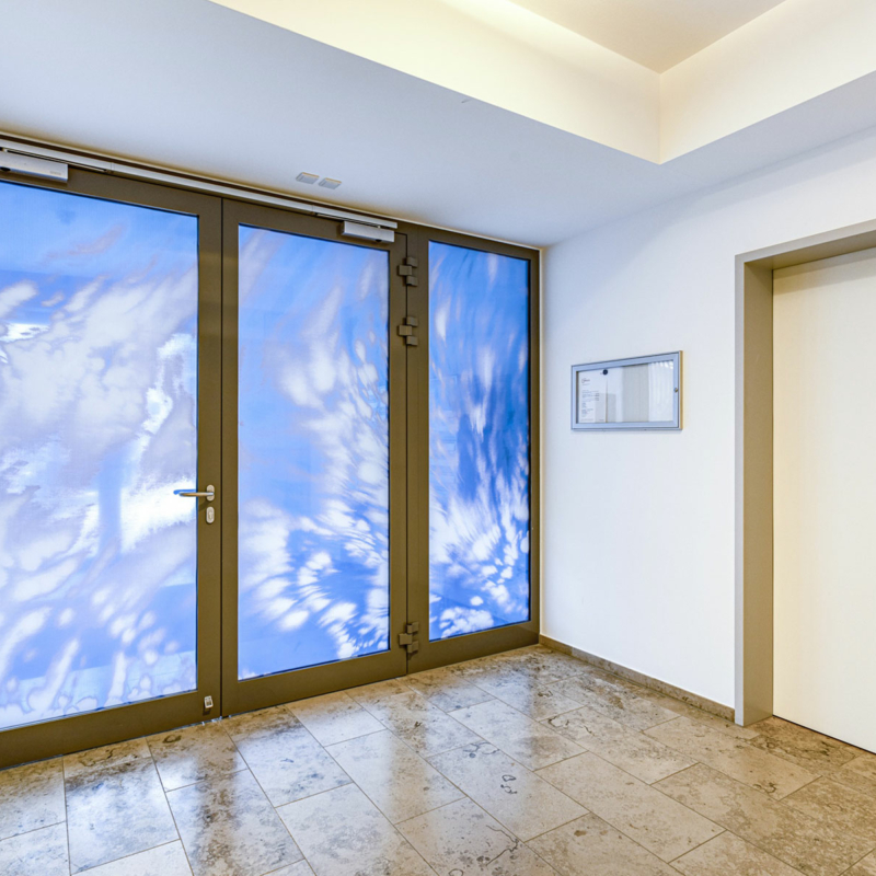 Eine gläserne Brandschutztür mit strahlendblauem Himmel und weißen Wolken bedruckt.