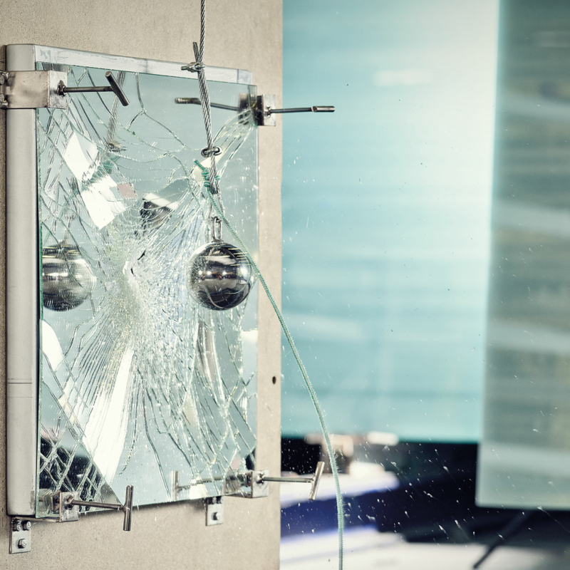 Versuchsaufbau: Ein Spiegel ist in Stücke zerbrochen, verursacht durch eine silberne Kugel (Pendel), die an einem Drahtseil hängt.