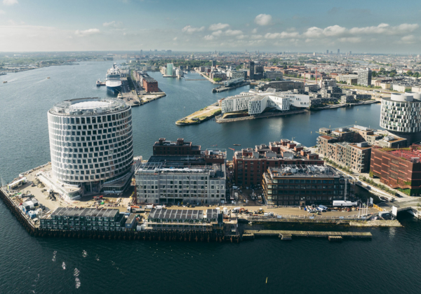 Luftbild des Kopenhagener Hafens mit vielen unterschiedlichen Gebäuden, in mehreren Ensembles im Wasser zu schwimmen scheinen. Im Bildmittelpunkt das kreisrunde Redmolen, ein Bürogebäude mit einer weißen Elementfassade.