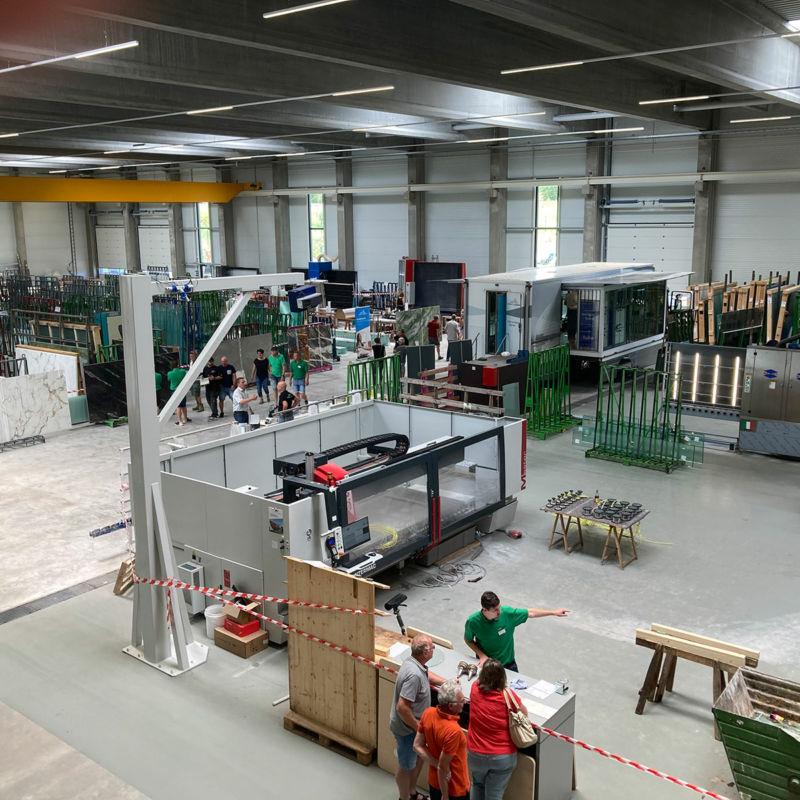 Blick in einen Produktionshalle mit Glasgestellen und Menschen, die auf hellgrauem Betonboden stehen
