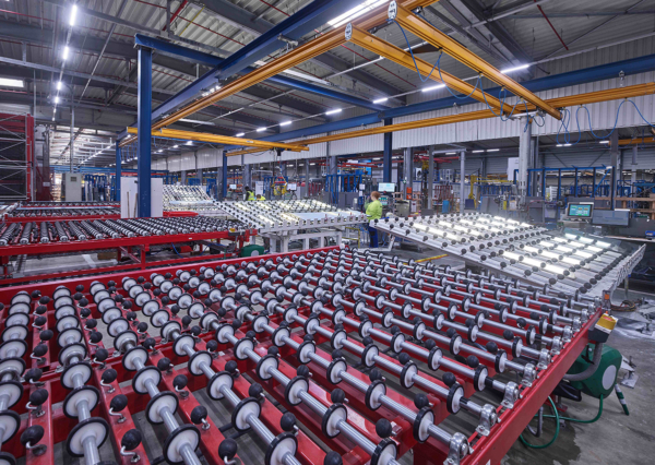 Blick in eine sehr große Halle, in der Glasscheiben verarbeitet werden, die über Rollen in großen Tischen gleiten