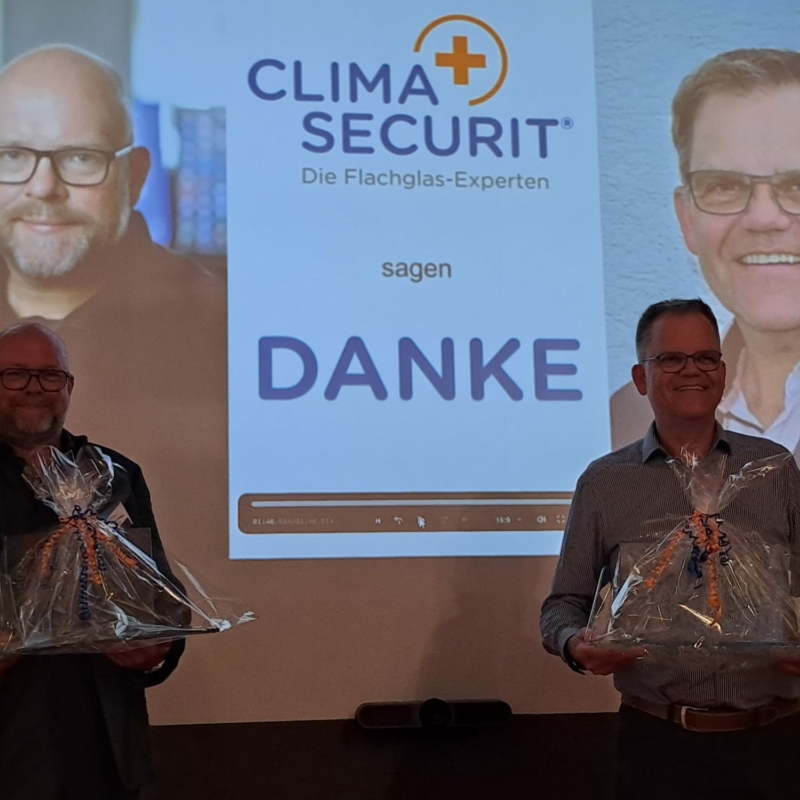 Frank Wulfmeier und Stefan Voth stehen vorne während ihrer Verabschiedung auf der CLIMAplusSECURIT-Jahrestagung 2025 in Frankfurt, während Vertreter von Saint-Gobain die Dankesrede halten.